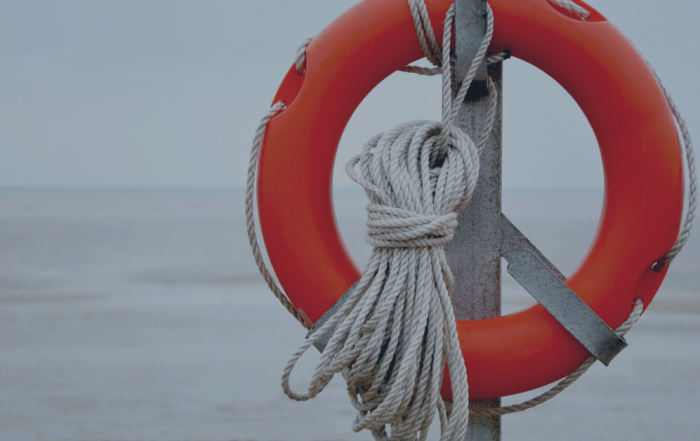 Advice for line managers: image depicts an orange life ring with rope wrapped around it in focus, with the sea in the distance behind out of focus.